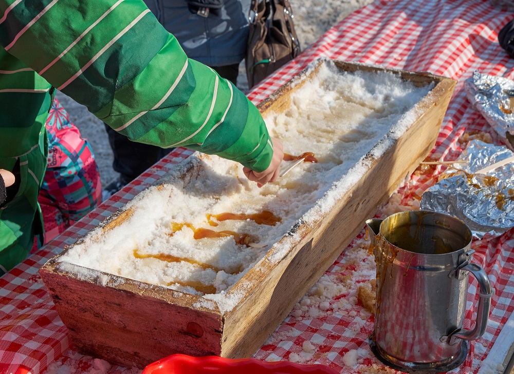 maple sugar snow candy - a child adding stick to candy
