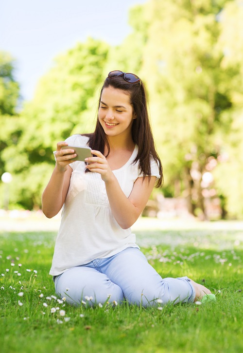 smiling young girl with smartphone sitting in park