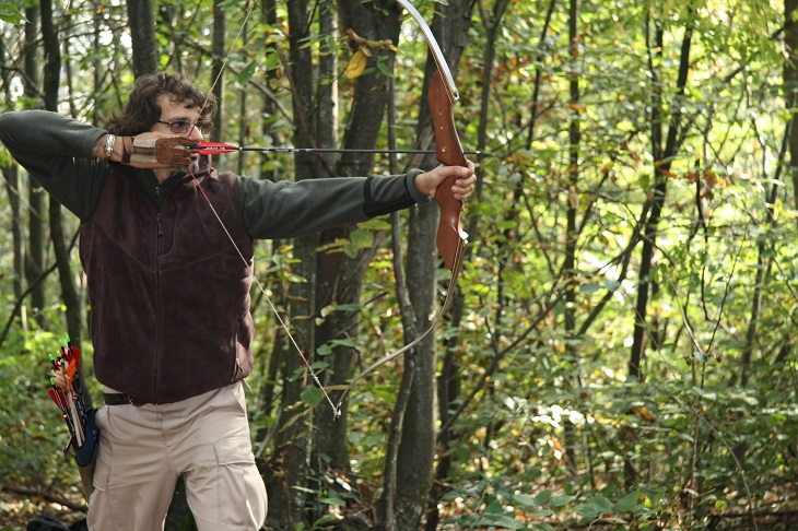 Man takes aim with a recurve bow in the forest