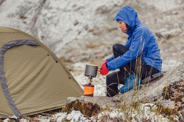 woman mountain climber boiling water on camp stove